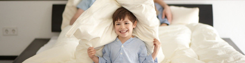 Ein Junge zieht sich im Bett ein Kopfkissen über den Kopf