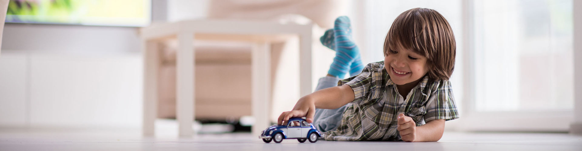 Ein kleines Kind liegt auf dem Fußboden und spielt mit einem Spielzeugauto.