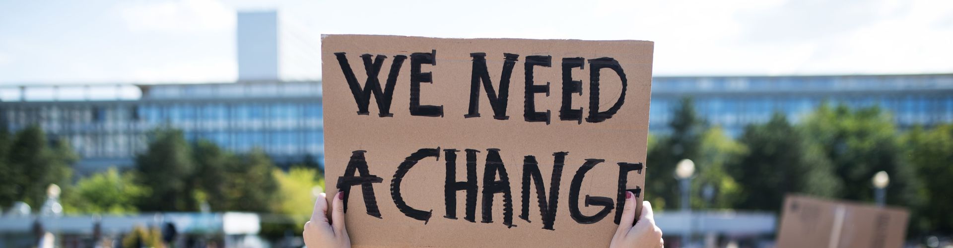 Protestlerin hält ein Schild in die Luft auf dem We Need A Change steht.