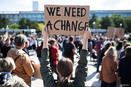 Protestlerin hält ein Schild in die Luft auf dem We Need A Change steht.