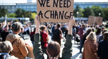 Protestlerin hält ein Schild in die Luft auf dem We Need A Change steht.
