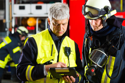 Zwei Feuerwehrleute, einer mit und einer ohne Helm, schauen auf ein Tablet