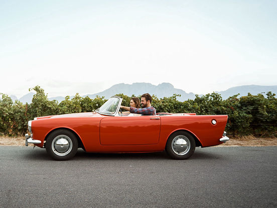 Ein Pärchen sitzt in einem roten Oldtimer-Cabrio.