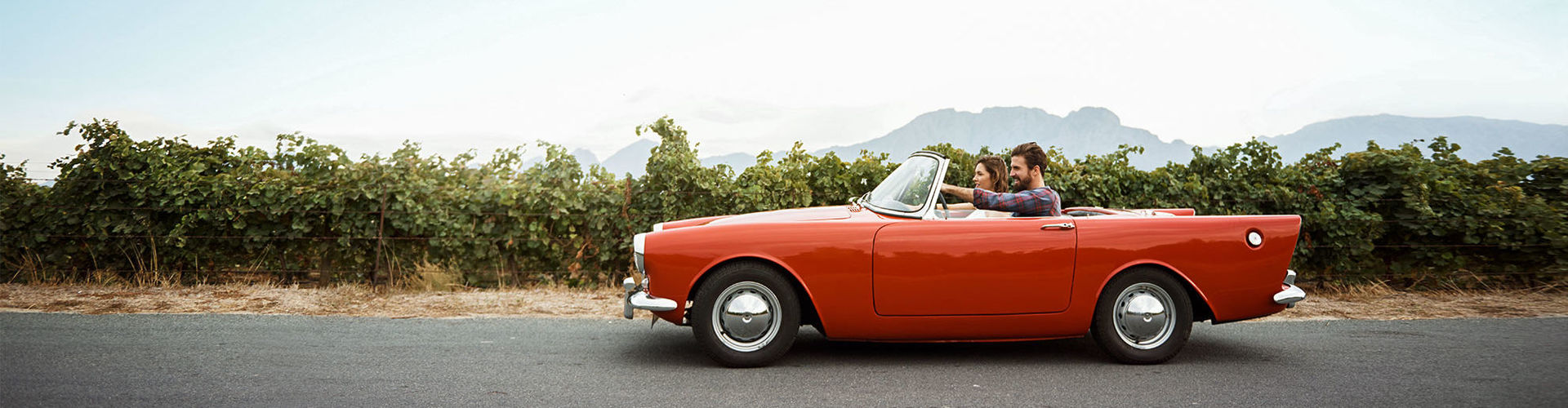 Ein Pärchen sitzt in einem roten Oldtimer-Cabrio.