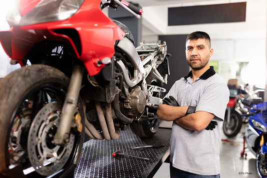 Mechaniker steht mit verschränkten Armen vor einem Motorrad.