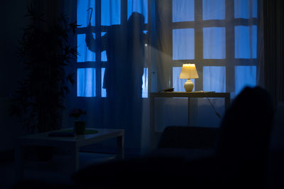 Person steht nachts am Fenster und schaut ins Haus.