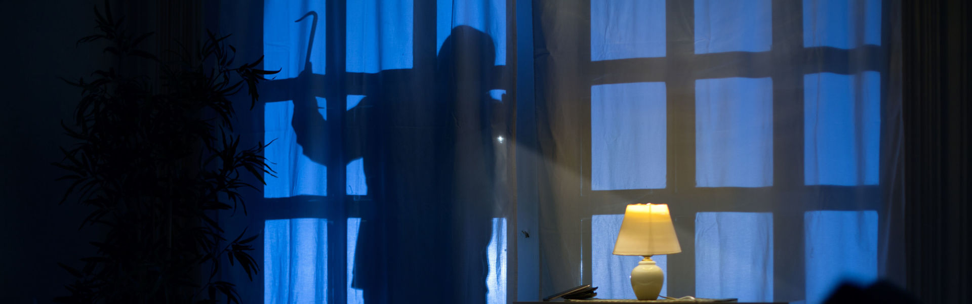 Person steht nachts am Fenster und schaut ins Haus.