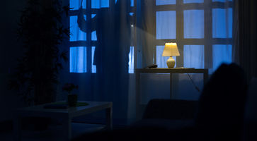 Person steht nachts am Fenster und schaut ins Haus.