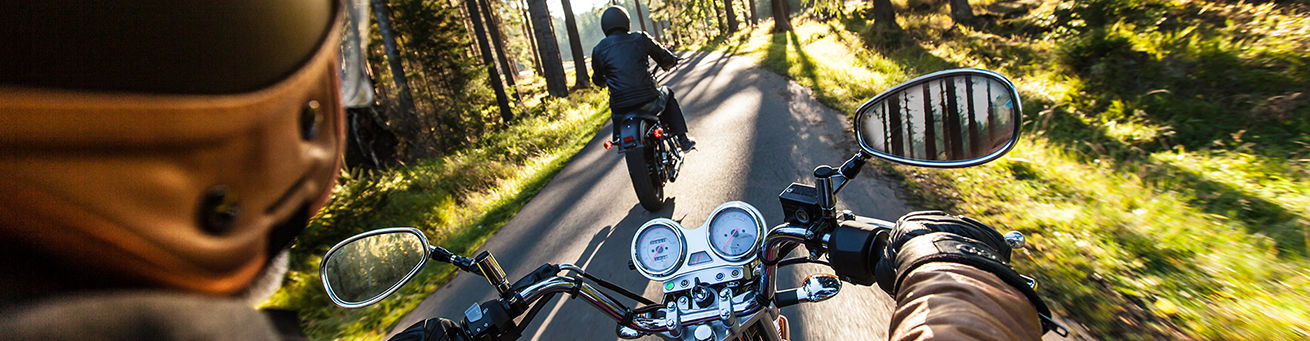 Zwei Personen fahren mit Motorrädern auf einer kleinen Straße im Wald.