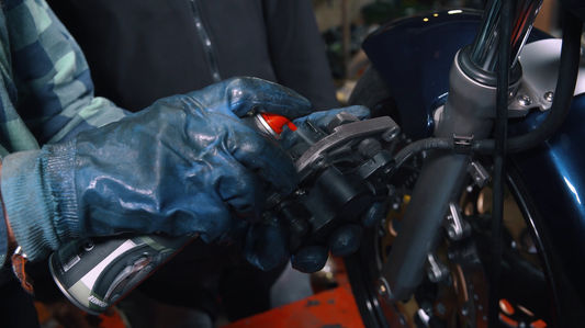 Eine Person reinigt einen Motorrad Bremsbelag mit Spray.