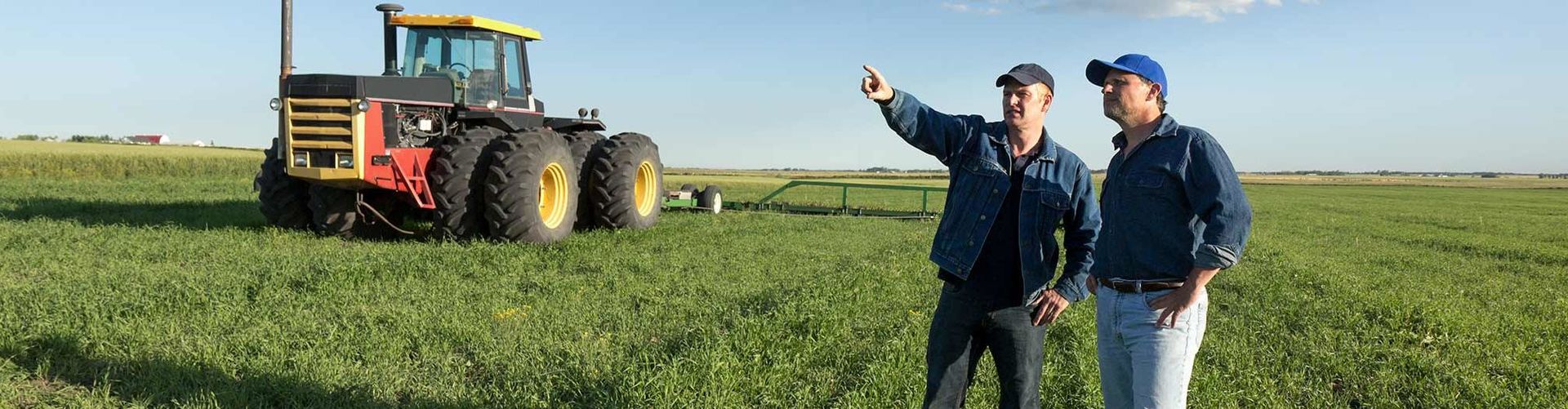 Zwei Landwirte auf einem Feld vor dem zu versichernden Traktor.