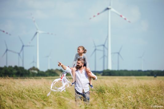 Ein Vater läuft mit seiner Tochter auf den Schultern über ein Feld.