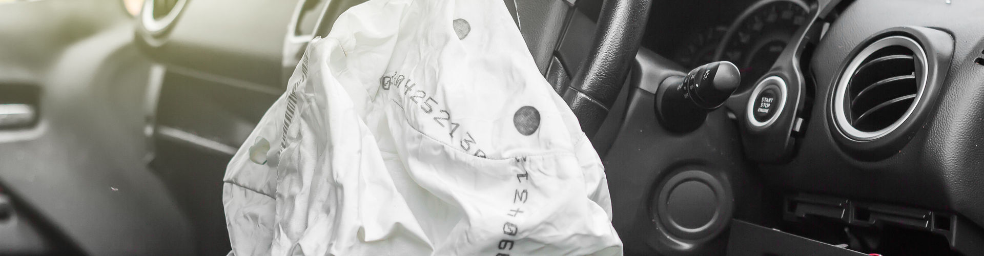 Ein ausgelöster Air Bag hängt aus dem Lenkrad eines Autos. Dahinter eine zersprungene Windschutzscheibe