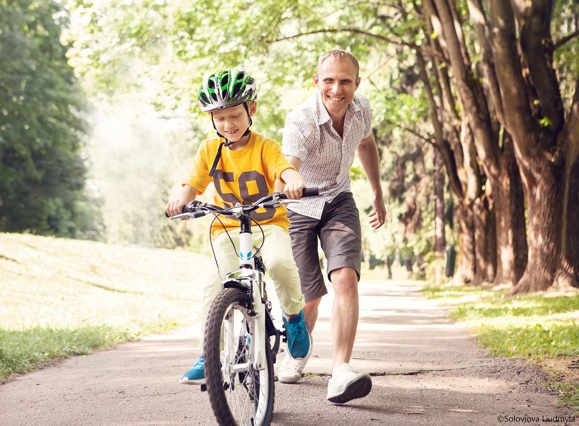 Vater hilft seinem Sohn beim Fahrrad fahren.